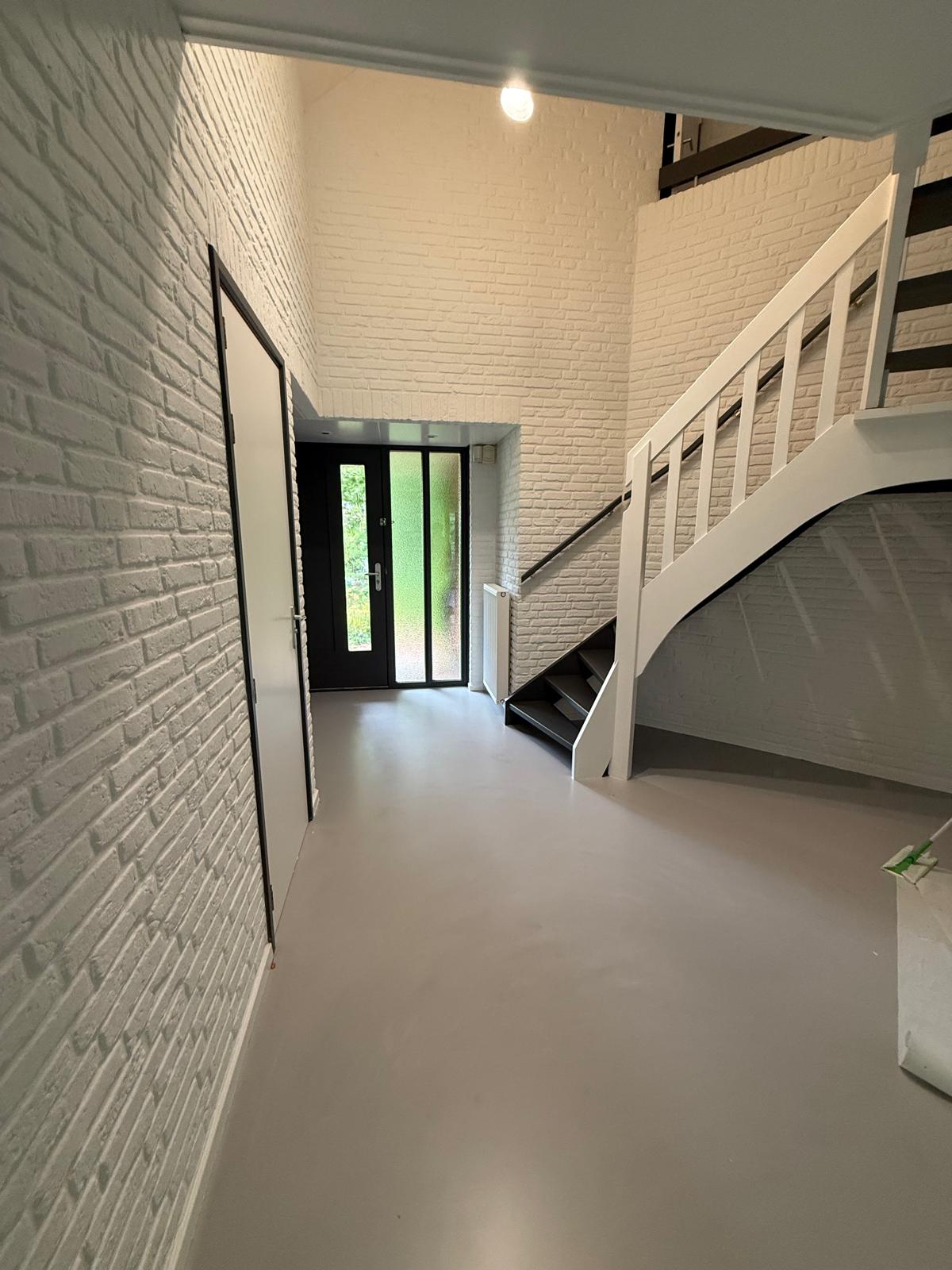 Strak geschilderde hal met witte trap en zwarte voordeur